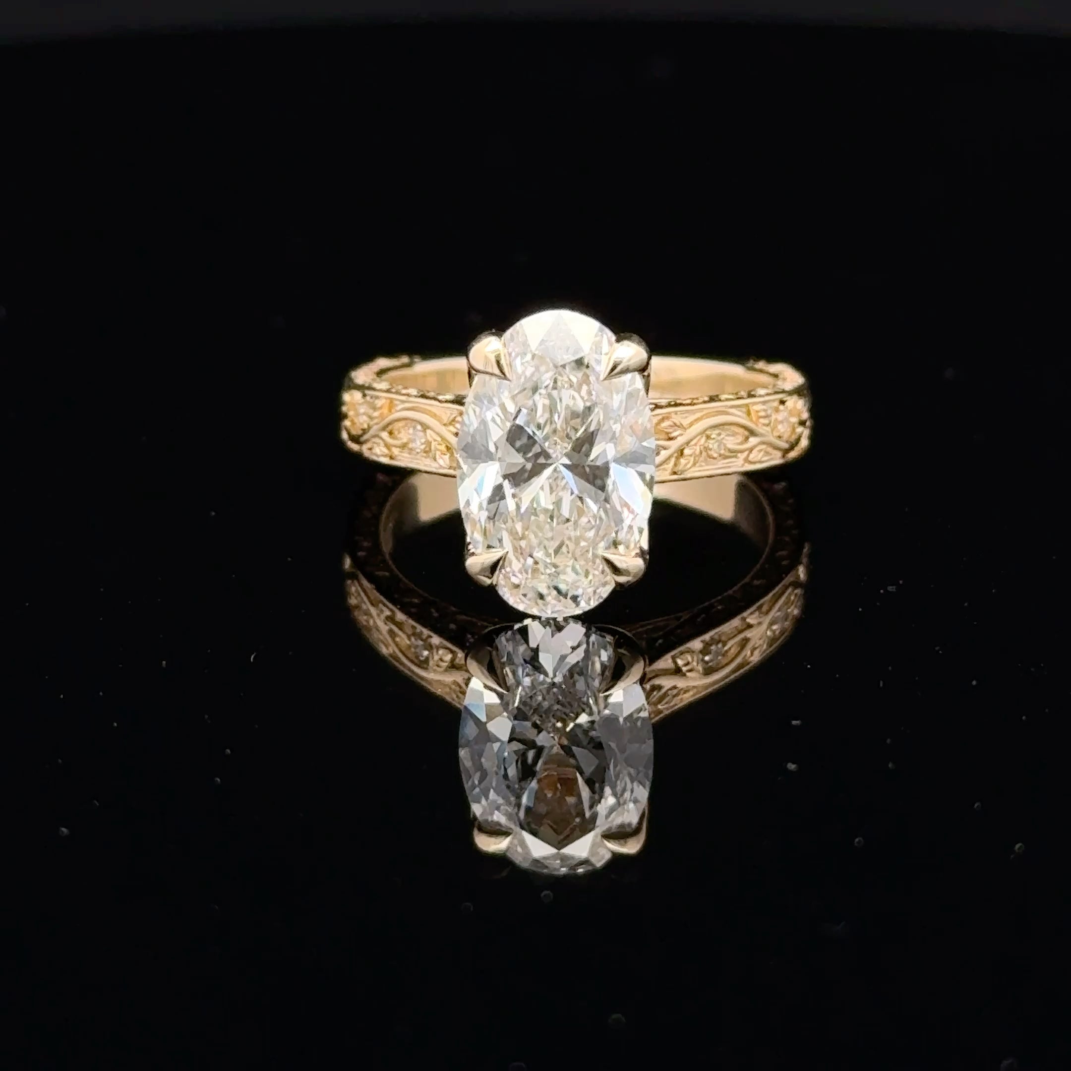 3 carat oval diamond ring with four claw prongs and a gold-toned band featuring winding vines, leaf details and small sparkling accents.