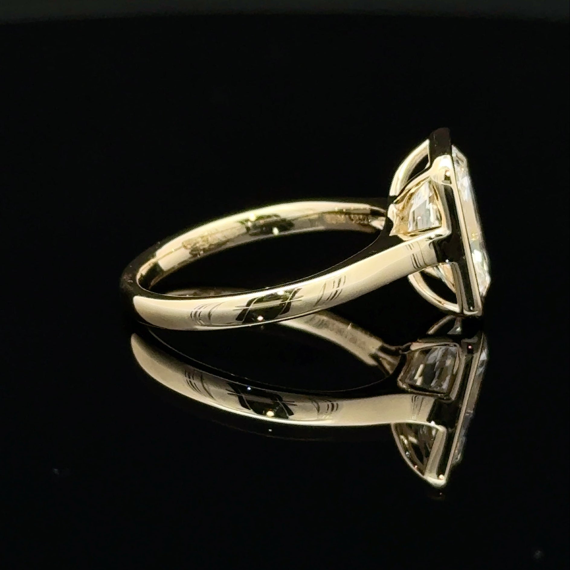 A yellow gold ring with a square bezel-set diamond, shown in profile on a reflective black surface.