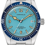 A Caravelle automatic dive watch with a stainless steel link bracelet, featuring a light blue dial, a dark blue bezel with white numerals, and gold-tone hands and indices.