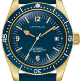 A Caravelle automatic dive watch with a gold-tone case, blue dial, and blue rubber strap, shown on a clean white background.
