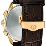 Close-up rear view of a wristwatch with a gold-tone case, silver-toned metal back, and dark brown leather strap with a gold clasp on a white background.