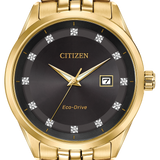 Citizen Eco-Drive watch with a gold-tone metal bracelet and case, featuring a dark charcoal gray dial with gold hands and hour markers.