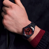 A close-up of a person's wrist wearing a black and red sports watch with a black metal bracelet, set against a dark jacket and red knit cuff.