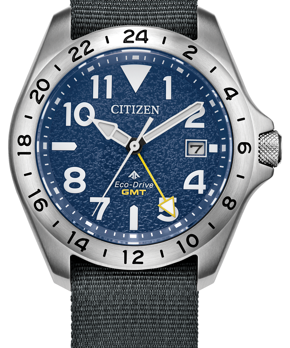 Citizen Eco-Drive GMT watch with a blue dial, silver-tone stainless steel case, and a dark gray woven fabric strap, shown on a plain white background.