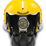 A wristwatch with a yellow and blue dial, displayed inside a yellow and black helmet-shaped presentation stand. The helmet features the text 'BLUE ANGELS' on the forehead.