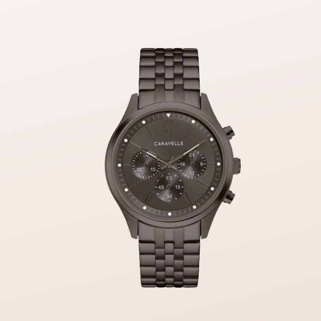 A Caravelle men's chronograph watch featuring a dark gunmetal gray case and a matching dark gray metal link bracelet, set against a solid off-white background.