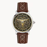 A gold-tone Texas Longhorn skull that symbolizes the enduring spirit of the West is set in relief against an ornate floral pattern inspired by the intricate decoration seen on traditional western wear.
