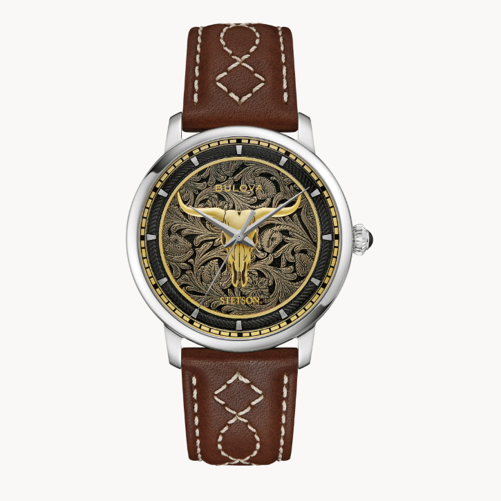 A gold-tone Texas Longhorn skull that symbolizes the enduring spirit of the West is set in relief against an ornate floral pattern inspired by the intricate decoration seen on traditional western wear.