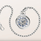 A silver pocket watch with a matching chain, featuring a skeleton dial with blue accents and a visible mechanical movement, set against a light beige background.