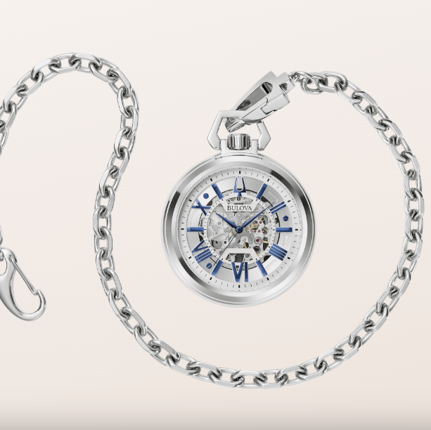 A silver pocket watch with a matching chain, featuring a skeleton dial with blue accents and a visible mechanical movement, set against a light beige background.