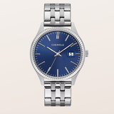 A luxury Caravelle wristwatch with a polished silver-tone stainless steel case and link bracelet, featuring a deep blue dial with gold-tone indices and a date window at the 3 o'clock position.