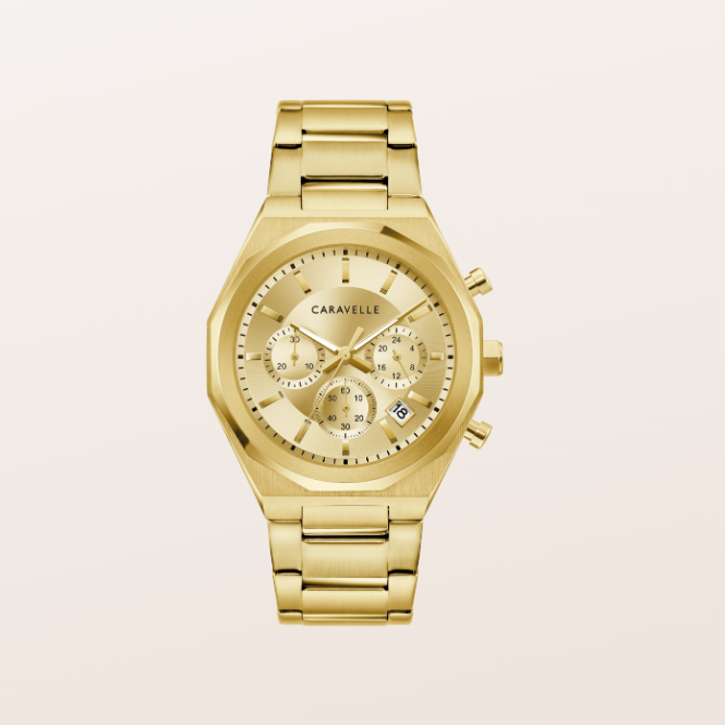 A gold-tone chronograph watch by Caravelle with a matching gold-tone metal link bracelet, shown against a light beige background.
