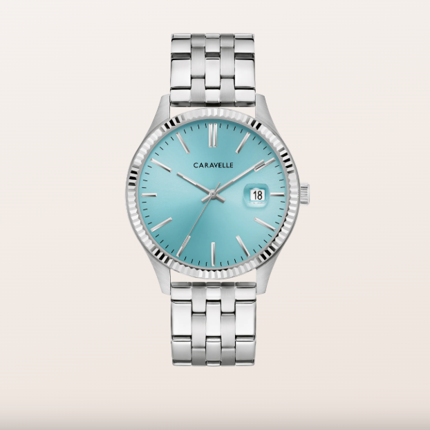 A Caravelle men's watch featuring a silver stainless steel bracelet and case, with a light turquoise blue dial and a date window at 3 o'clock, set against a solid light beige background.