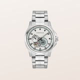 A silver-tone stainless steel wristwatch with a multi-link bracelet, featuring a skeletonized white dial with a visible mechanical movement and a gray subdial, shown against a solid light beige background.