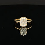 A yellow gold ring featuring a cushion-cut diamond, displayed on a reflective black surface.