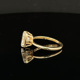 A yellow gold ring with a rectangular clear gemstone in a four-prong setting, displayed on a reflective black surface against a dark gray background.