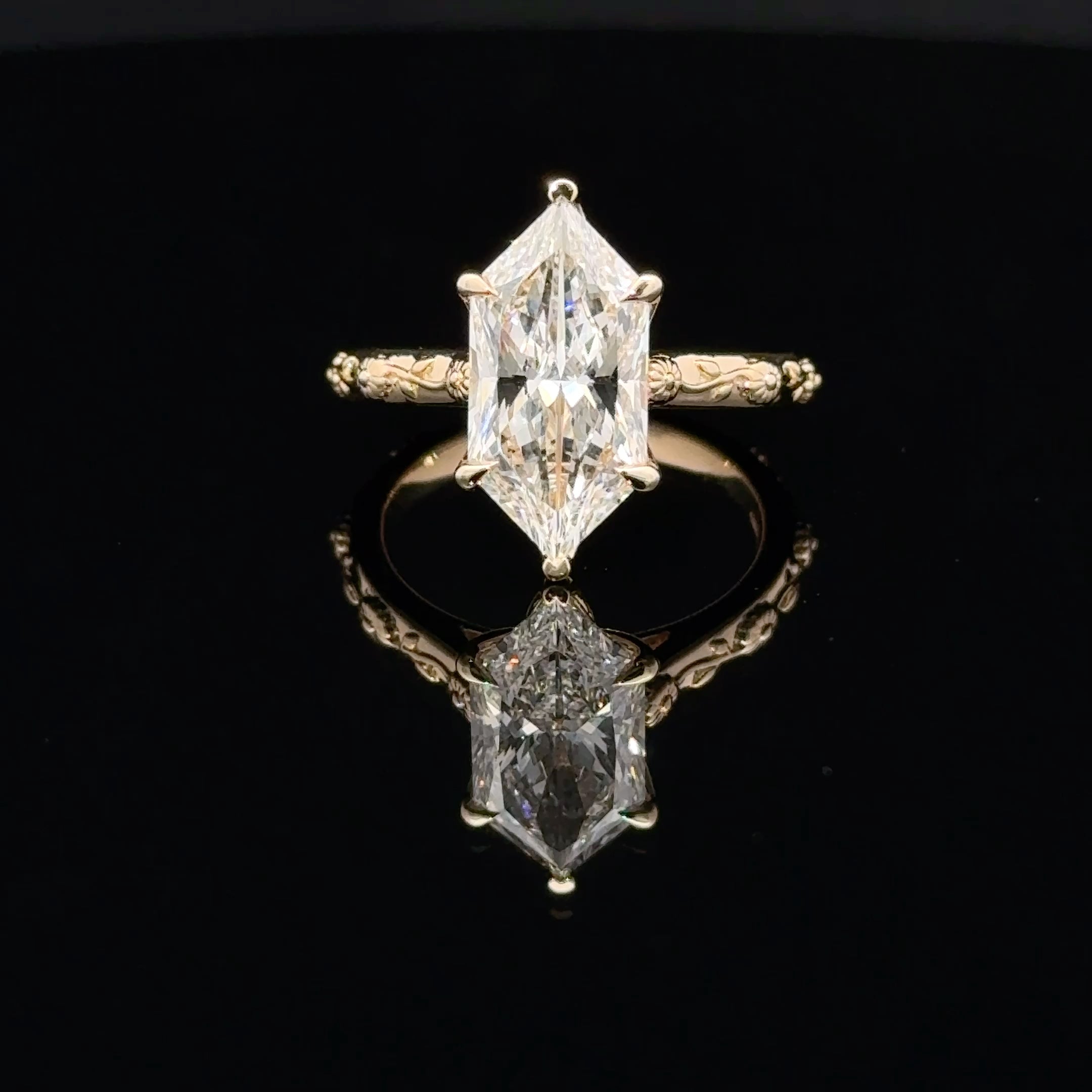 A yellow gold ring featuring a large marquise-cut clear gemstone in a prong setting, with an ornate shank, displayed on a reflective black surface.