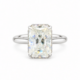 An emerald-cut diamond ring with a silver-toned band and a halo of small diamonds, centered on a plain white background.