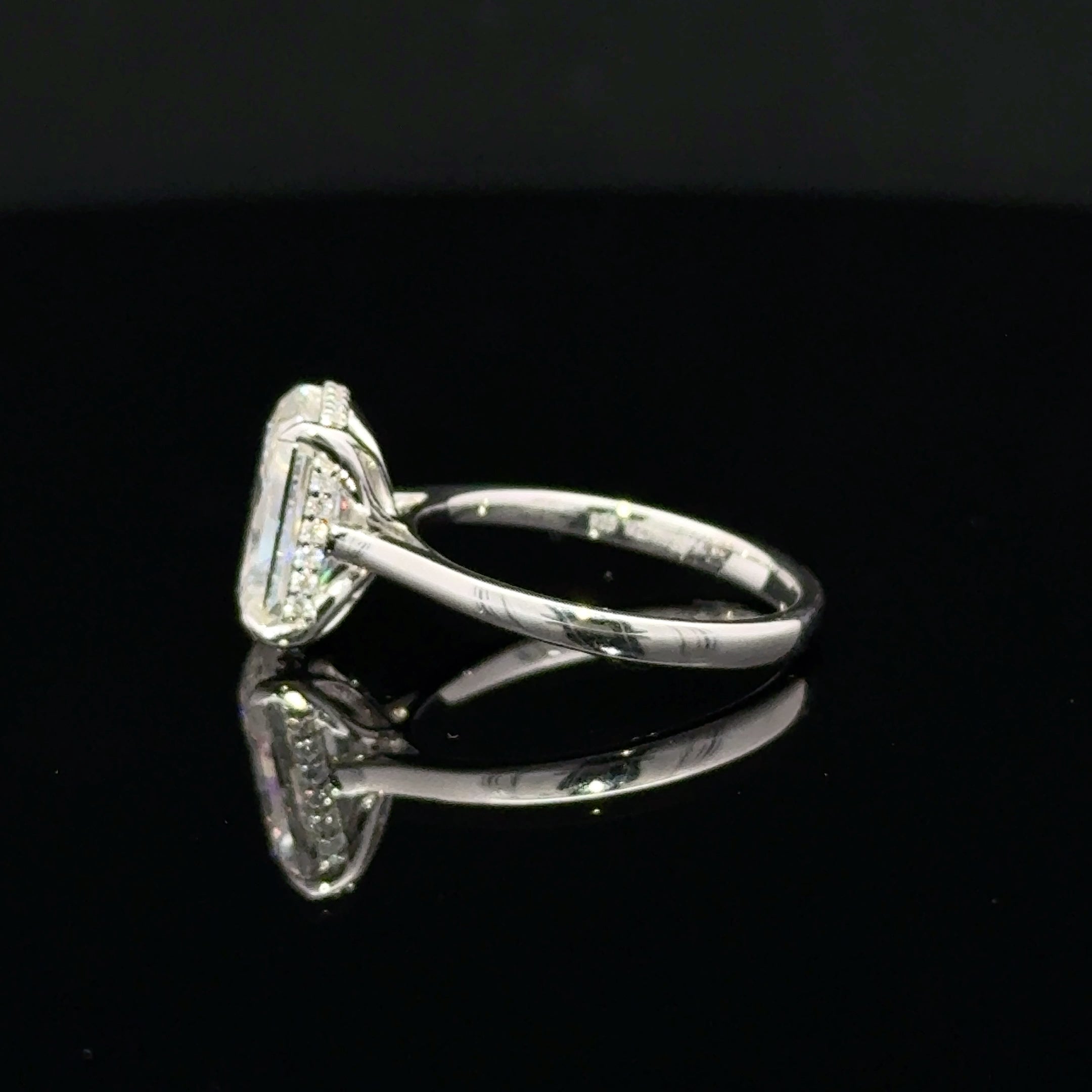 A silver ring with a rectangular pavé diamond setting, shown from a side angle on a reflective black surface.