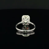 A silver ring with radiant-cut clear gemstone in a decorative setting, displayed on a reflective black surface.