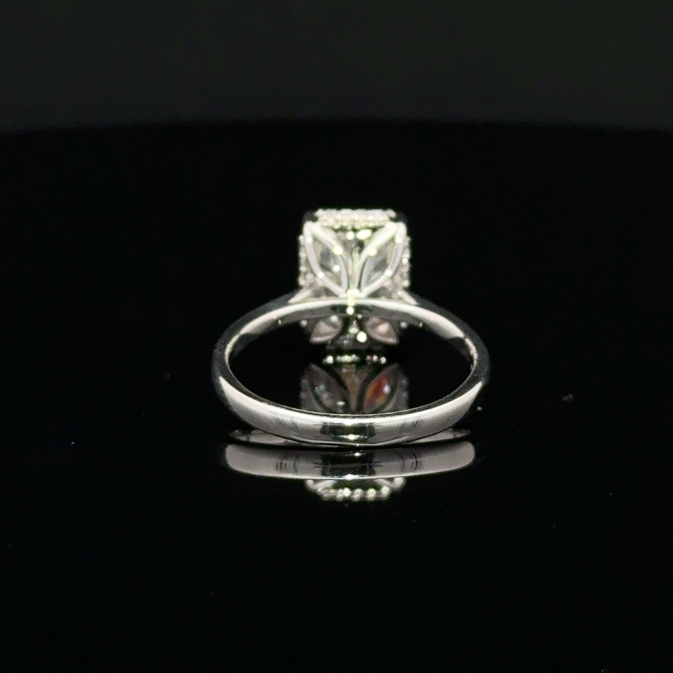 A silver ring with radiant-cut clear gemstone in a decorative setting, displayed on a reflective black surface.