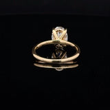 A yellow gold ring with a clear gemstone in a prong setting, displayed on a reflective black surface against a dark background.