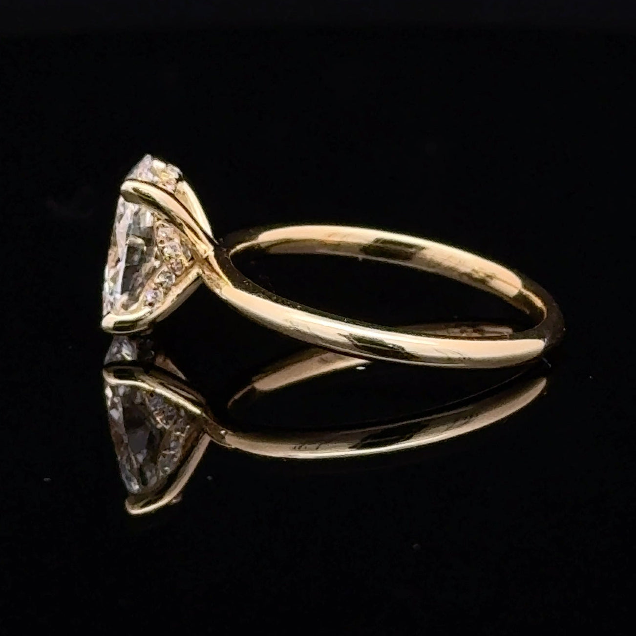 A yellow gold ring featuring a oval-cut diamond in a prong setting, displayed on a reflective black surface.