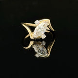 A yellow gold ring featuring a marquise-cut diamond center stone with smaller round diamonds on the shoulders, displayed on a reflective black surface.