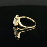 A yellow gold ring with a large clear gemstone in a prong setting, displayed on a reflective black surface.