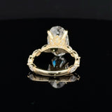 A yellow gold ring with a large clear oval gemstone in a prong setting, displayed on a reflective black surface.