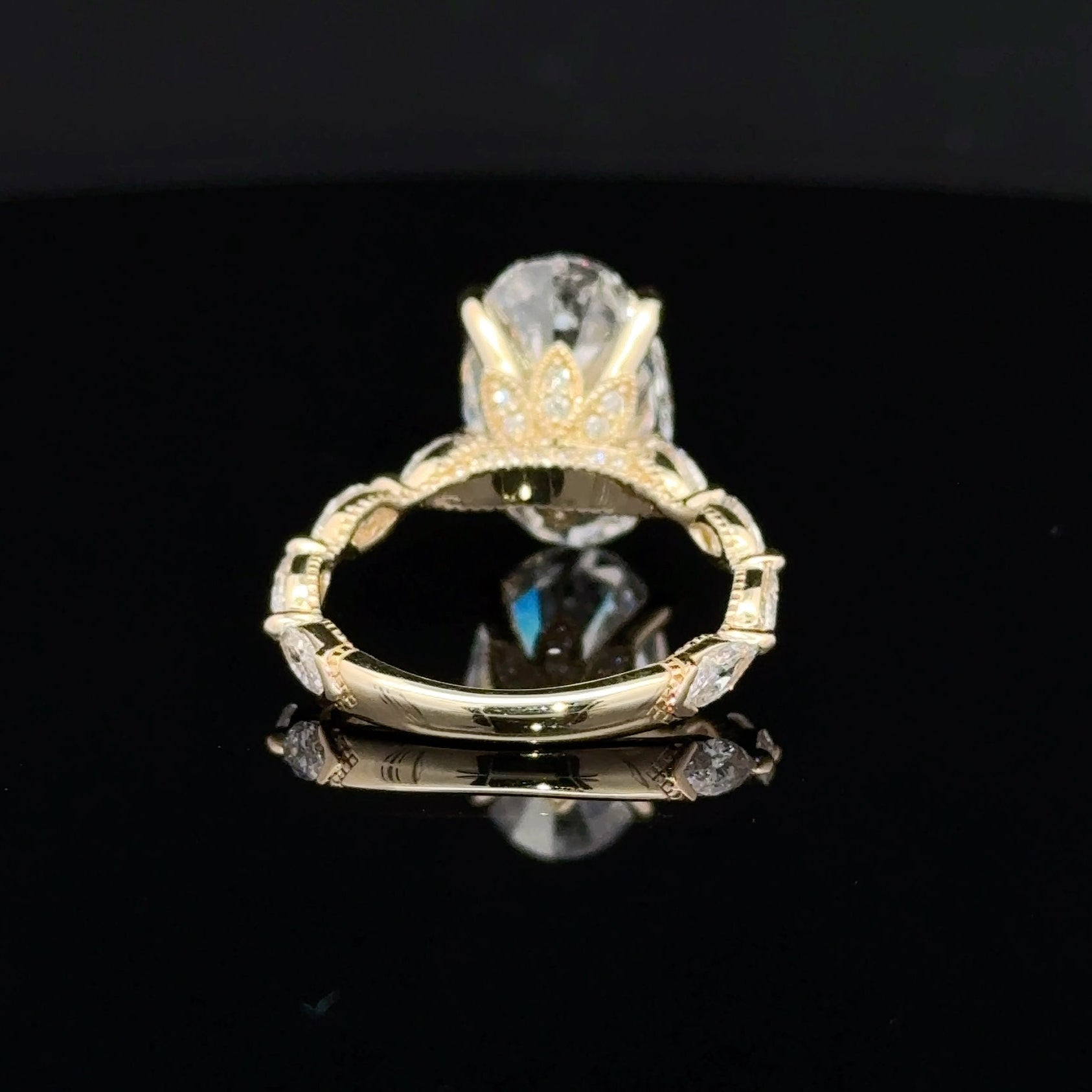 A yellow gold ring with a large clear oval gemstone in a prong setting, displayed on a reflective black surface.