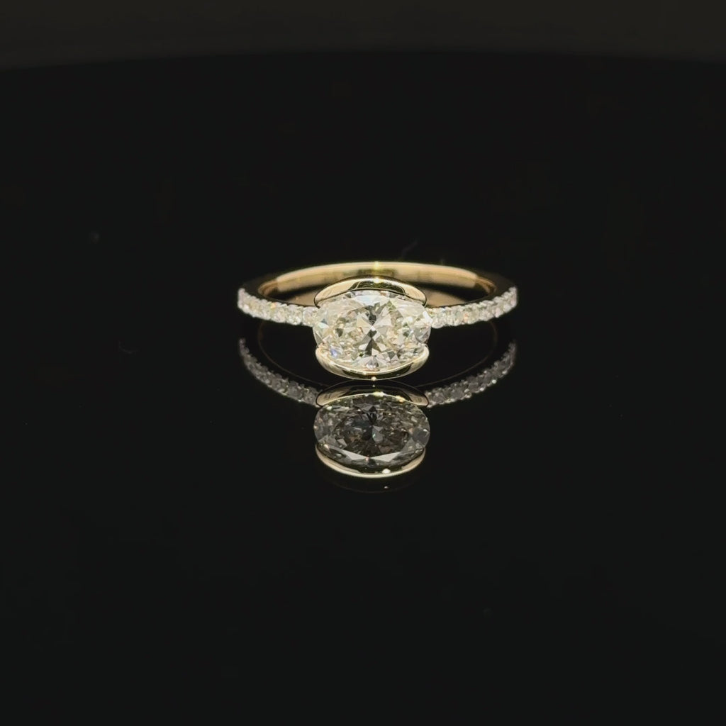 Horizontal oval diamond ring with curved half-bezel edges and a slender sparkling accent band.