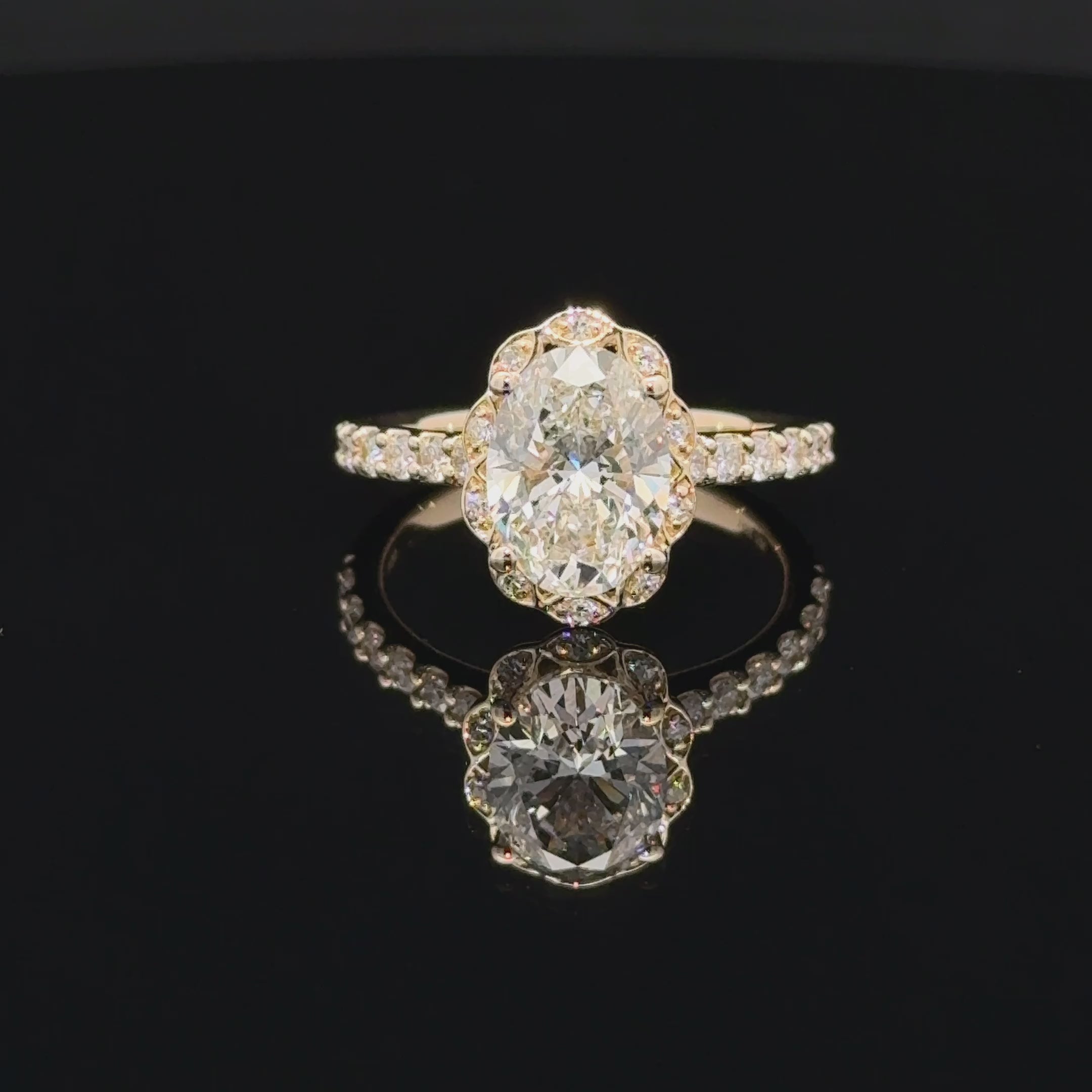 Oval diamond ring with a scalloped halo, four rounded prongs and a slender sparkling accent band.
