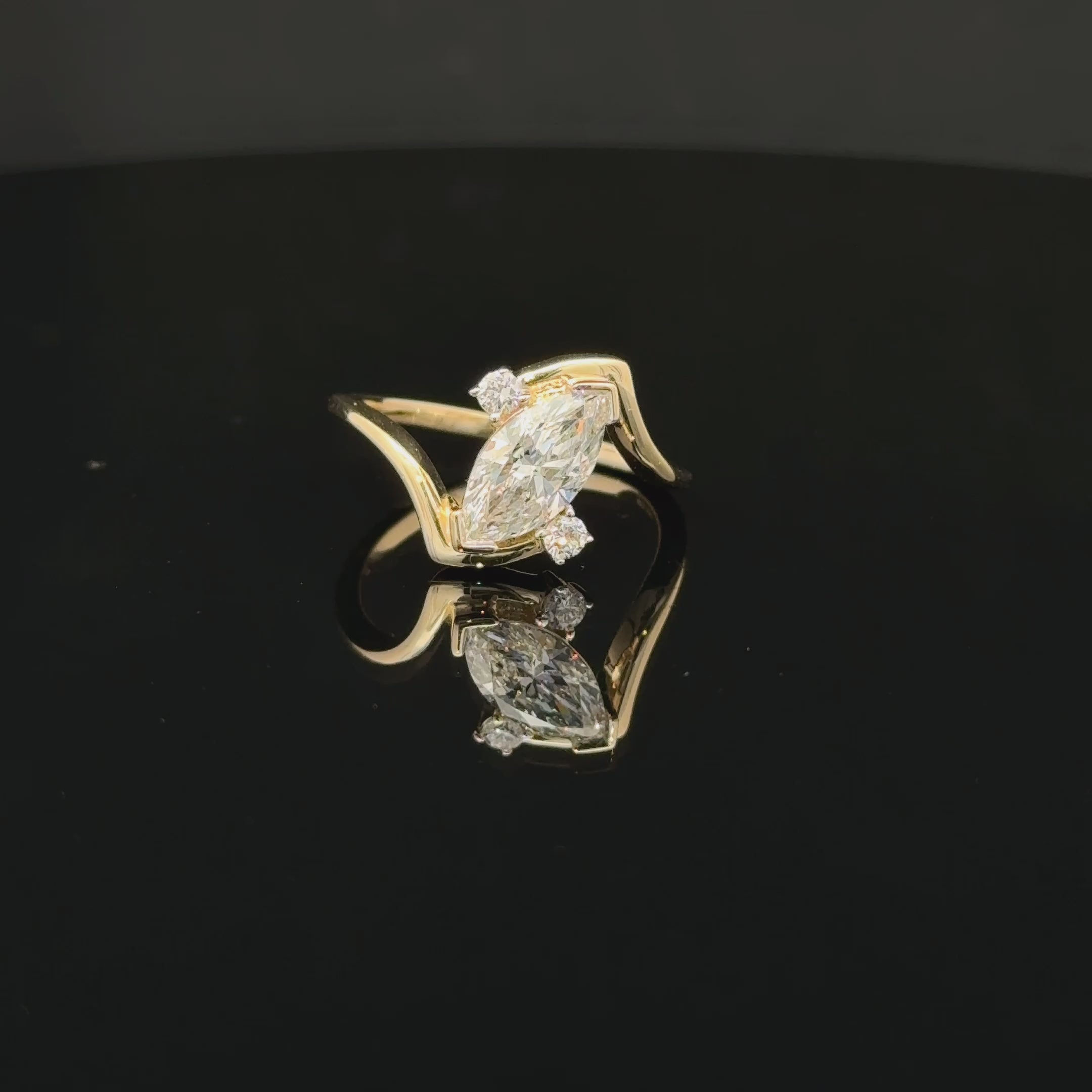 Diagonal marquise diamond ring with two round accents and a sweeping gold-toned bypass band.
