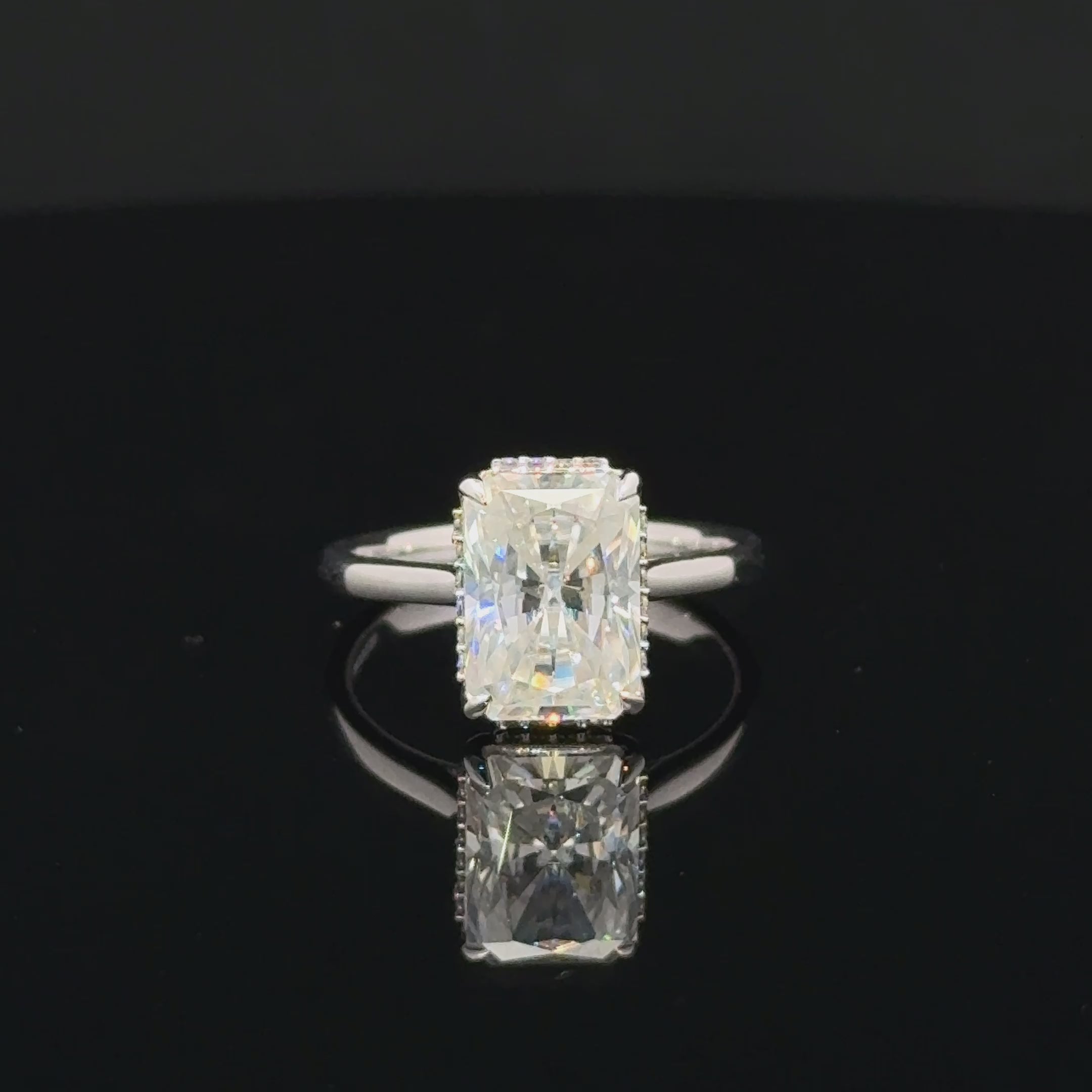 Rectangular moissanite ring in polished silver with four claw prongs, small setting accents and a plain band.