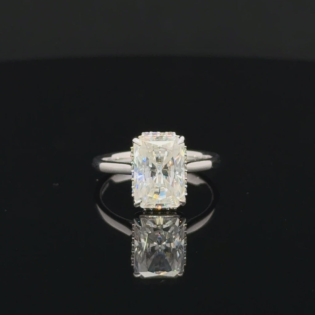 Rectangular moissanite ring in polished silver with four claw prongs, small setting accents and a plain band.