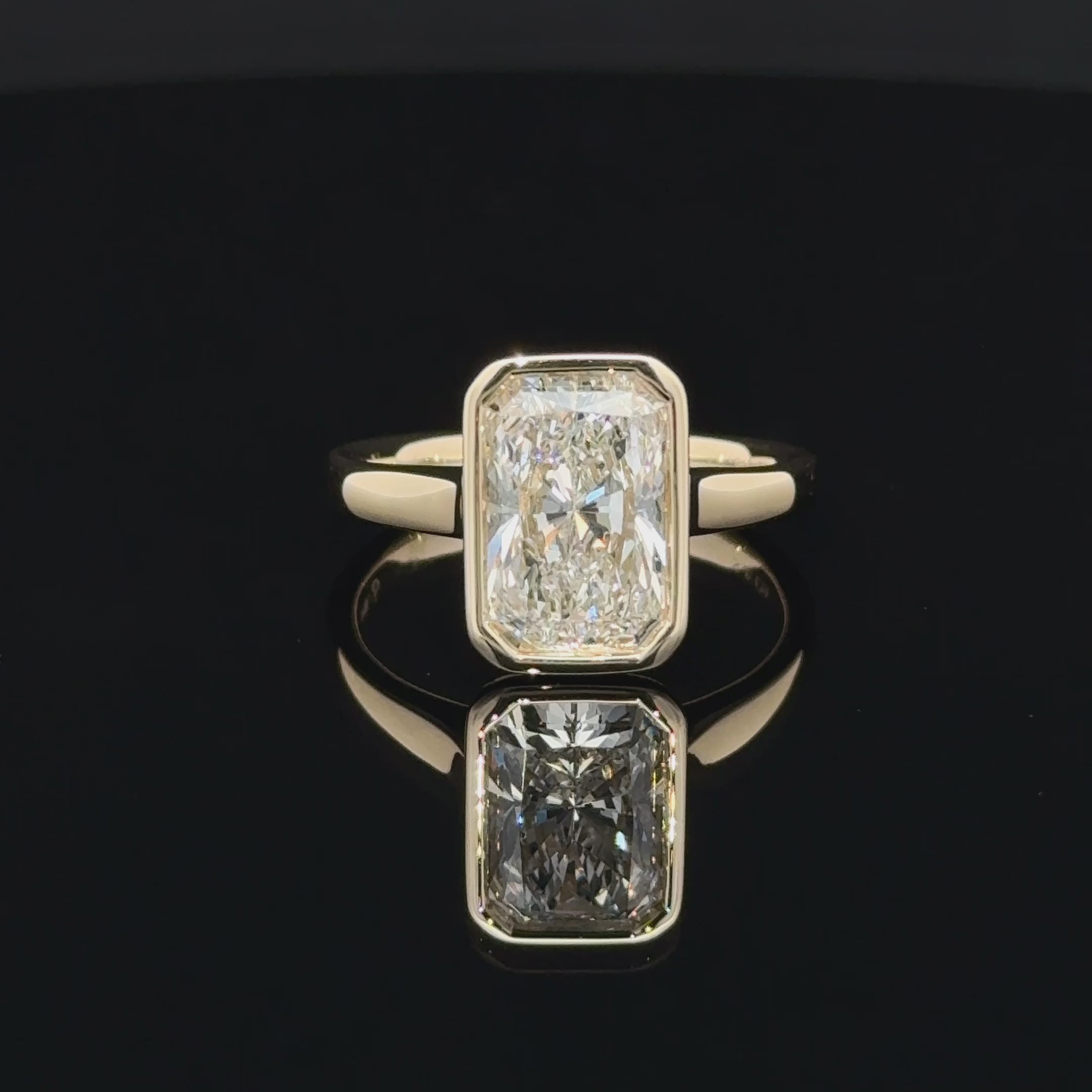 Front view of a 3 carat rectangular radiant-cut diamond in a smooth yellow-gold-toned bezel setting with a polished plain band.