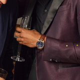 Person in a purple suit holding a glass of champagne with a watch on their wrist.